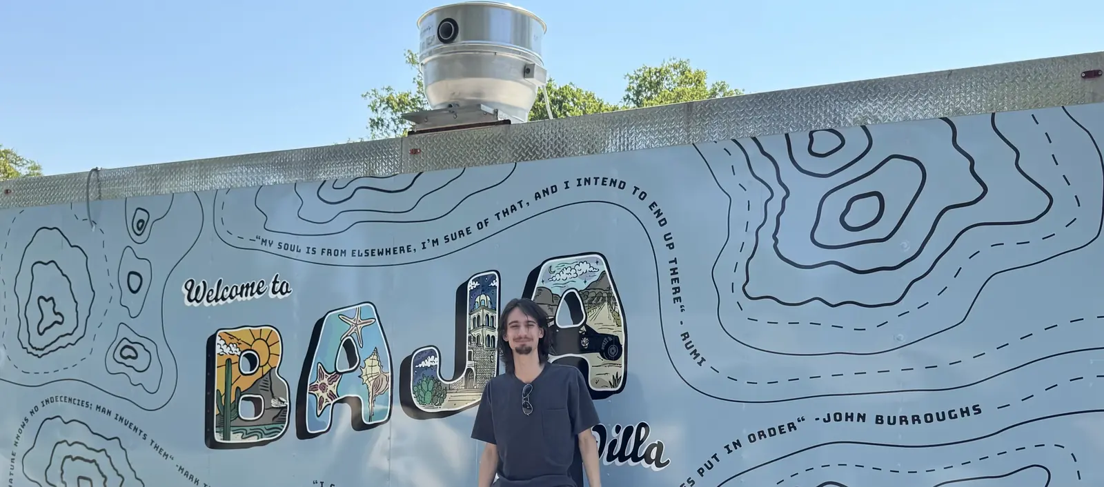 Jack standing in front of the Baja Quesadilla trailer and its topographic wrap