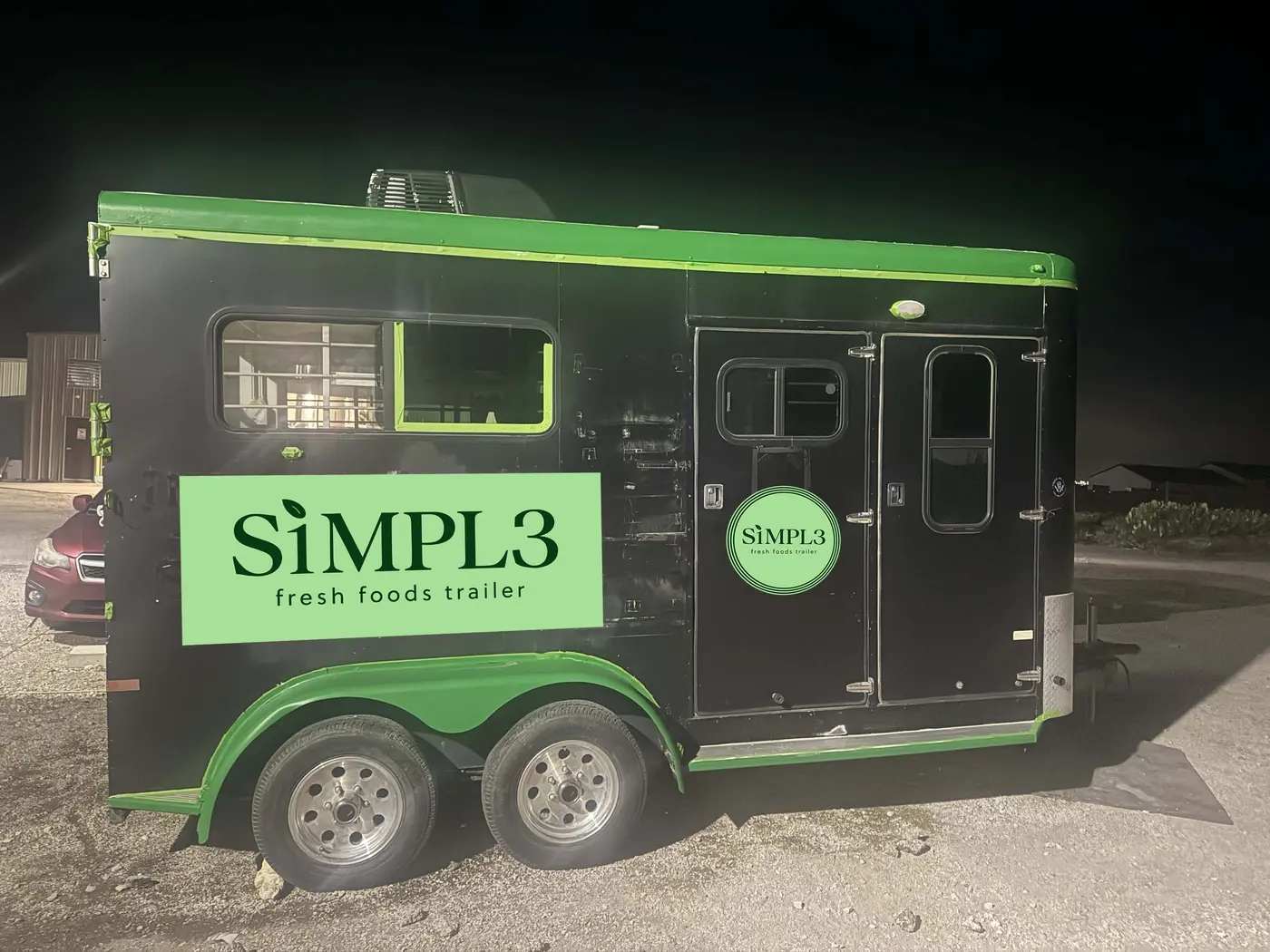 Black SiMPL3 fresh foods trailer with green trim and logo panels, photographed at night